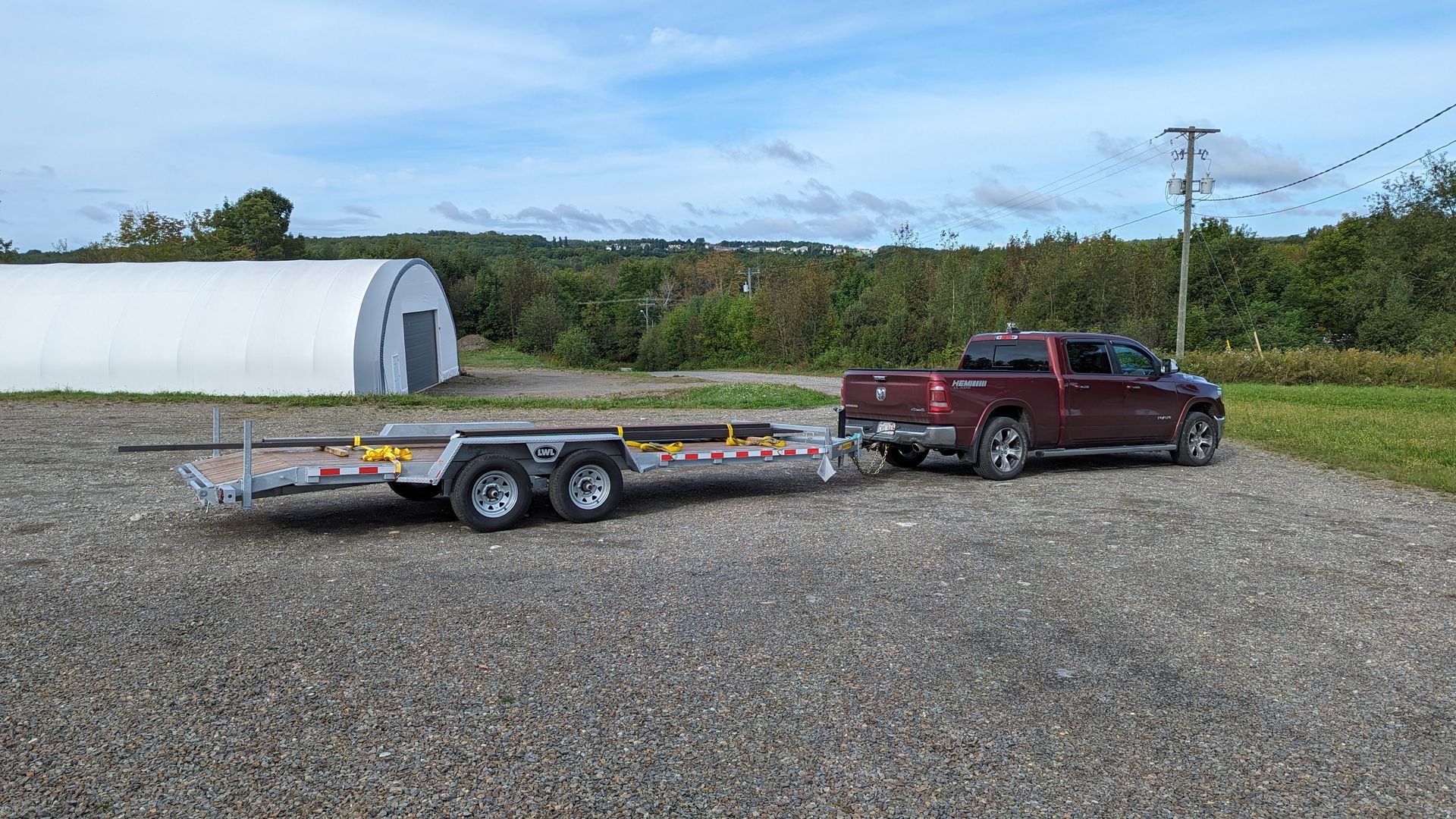 A red truck is towing a trailer in a gravel lot.