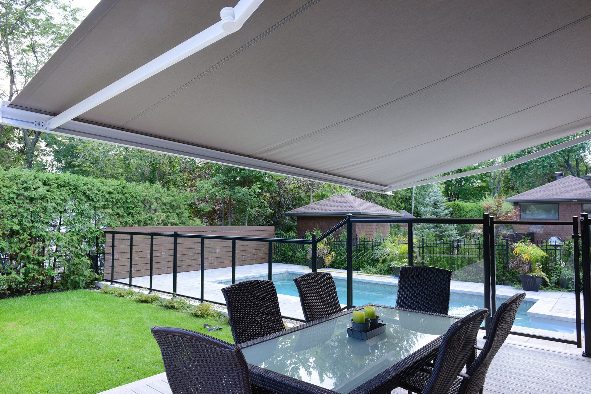 A patio with a table and chairs under an awning next to a pool.