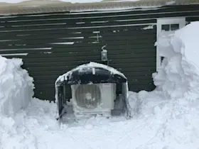 An air conditioner is covered in snow in front of a house.