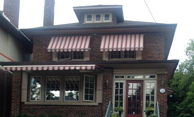 A brick house with red and white awnings on the windows.