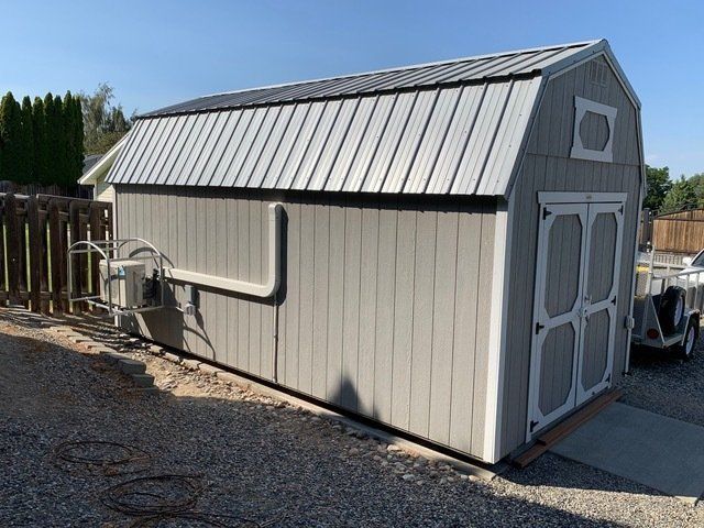 A barn shaped shed with a metal roof is parked in a gravel lot.