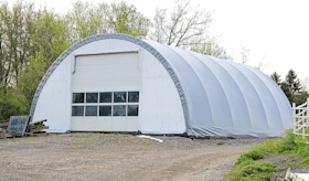 A large white building with a garage door is sitting in the middle of a dirt field.