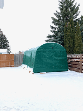 A green tent is sitting in the snow next to a wooden fence.