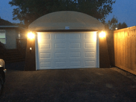 A car is parked in front of a garage that is lit up at night