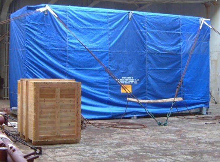 A blue tarp is covering a wooden box in a warehouse