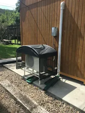 A small air conditioner is sitting outside of a wooden building.
