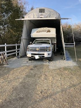 A white truck is parked under a tent in a gravel lot.