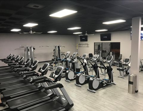 Gym interior with rows of treadmills, elliptical machines, and weight equipment.