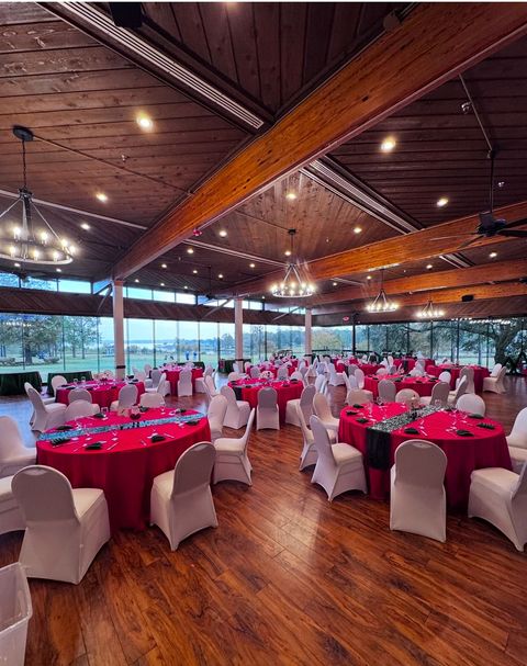 Event hall with red tablecloths, white chairs, wooden floor and ceiling.