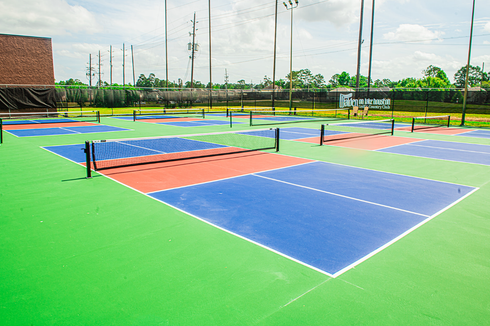 Outdoor pickleball courts with blue, red, and green surfaces, net, and fences.