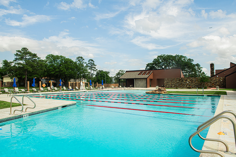 Swimming pool with lane lines, lounge chairs, and a building in the background under a blue sky.