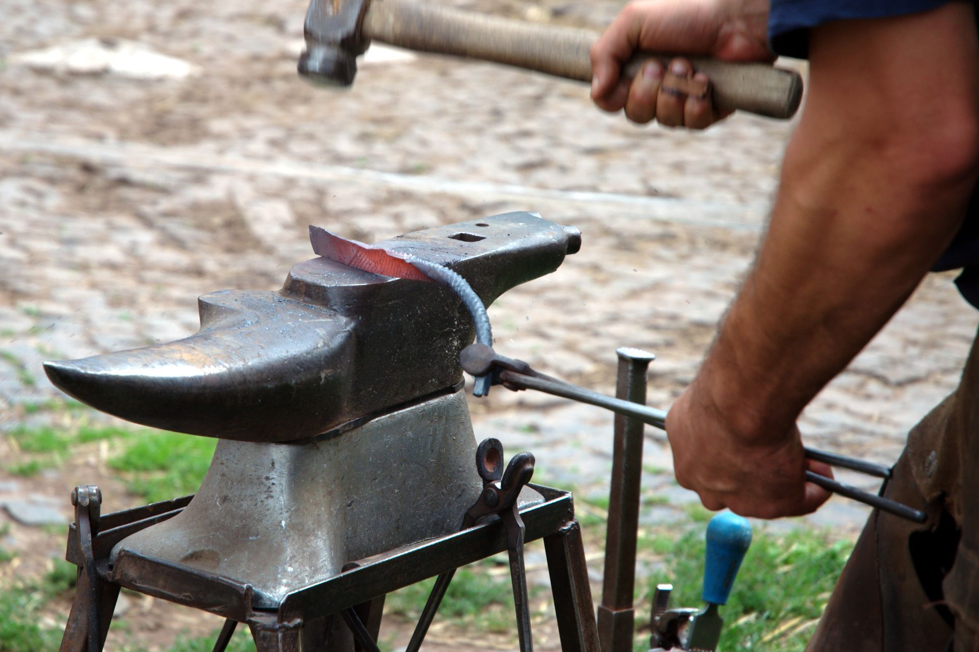 Blacksmith hammering red-hot metal on an anvil, shaping it with tongs.