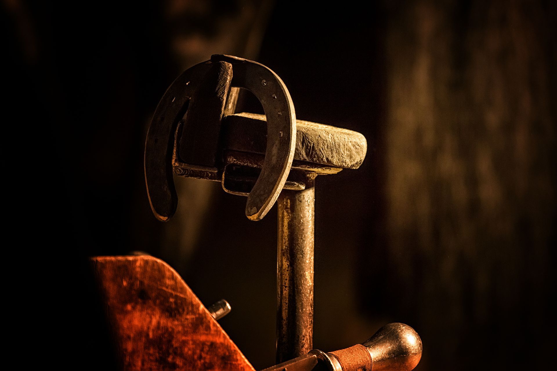 Horseshoe on a farrier's stand in dim lighting, showing blacksmithing tools.