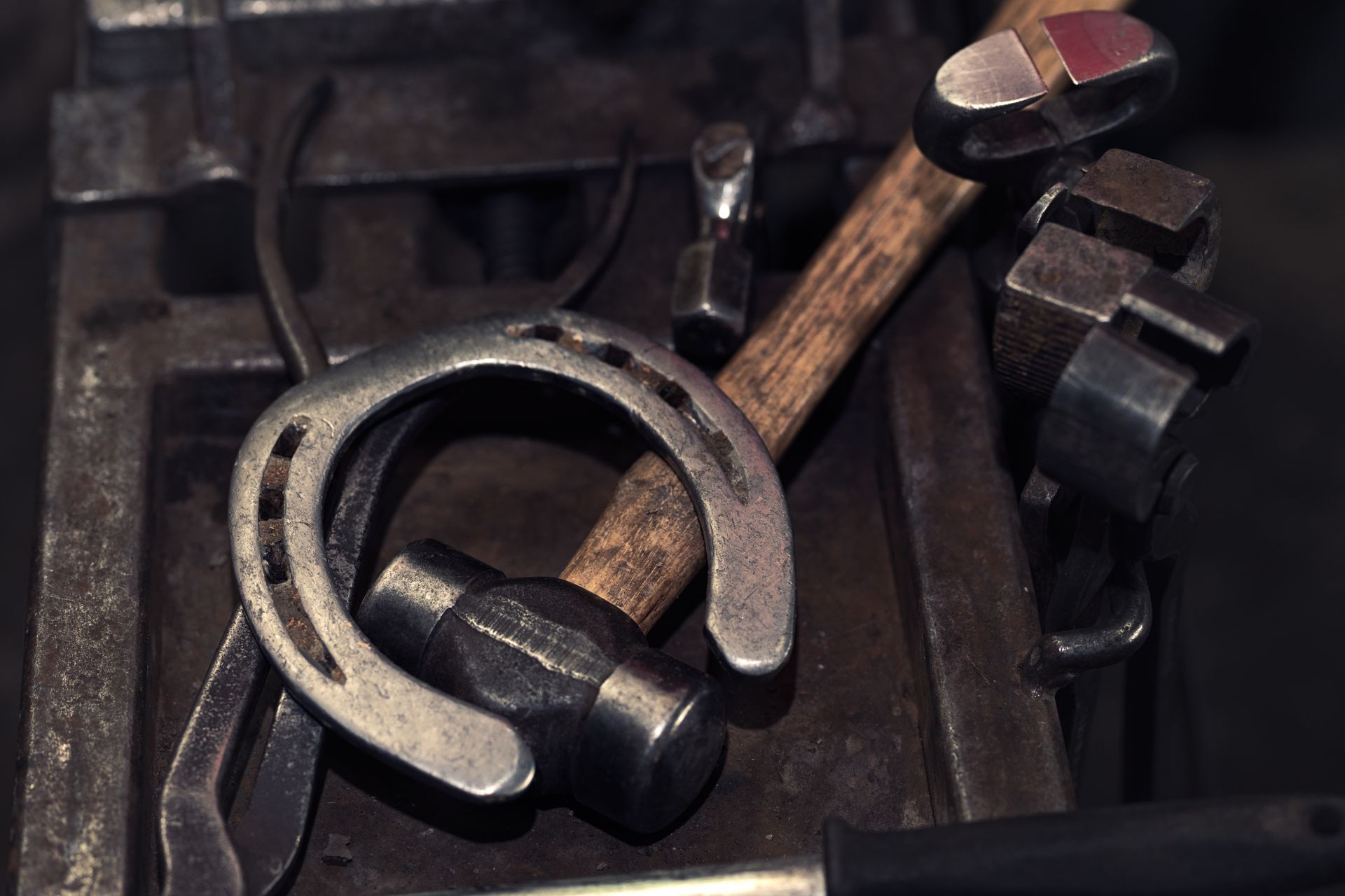 Horseshoe, hammer, and tools on a blacksmith's workbench.