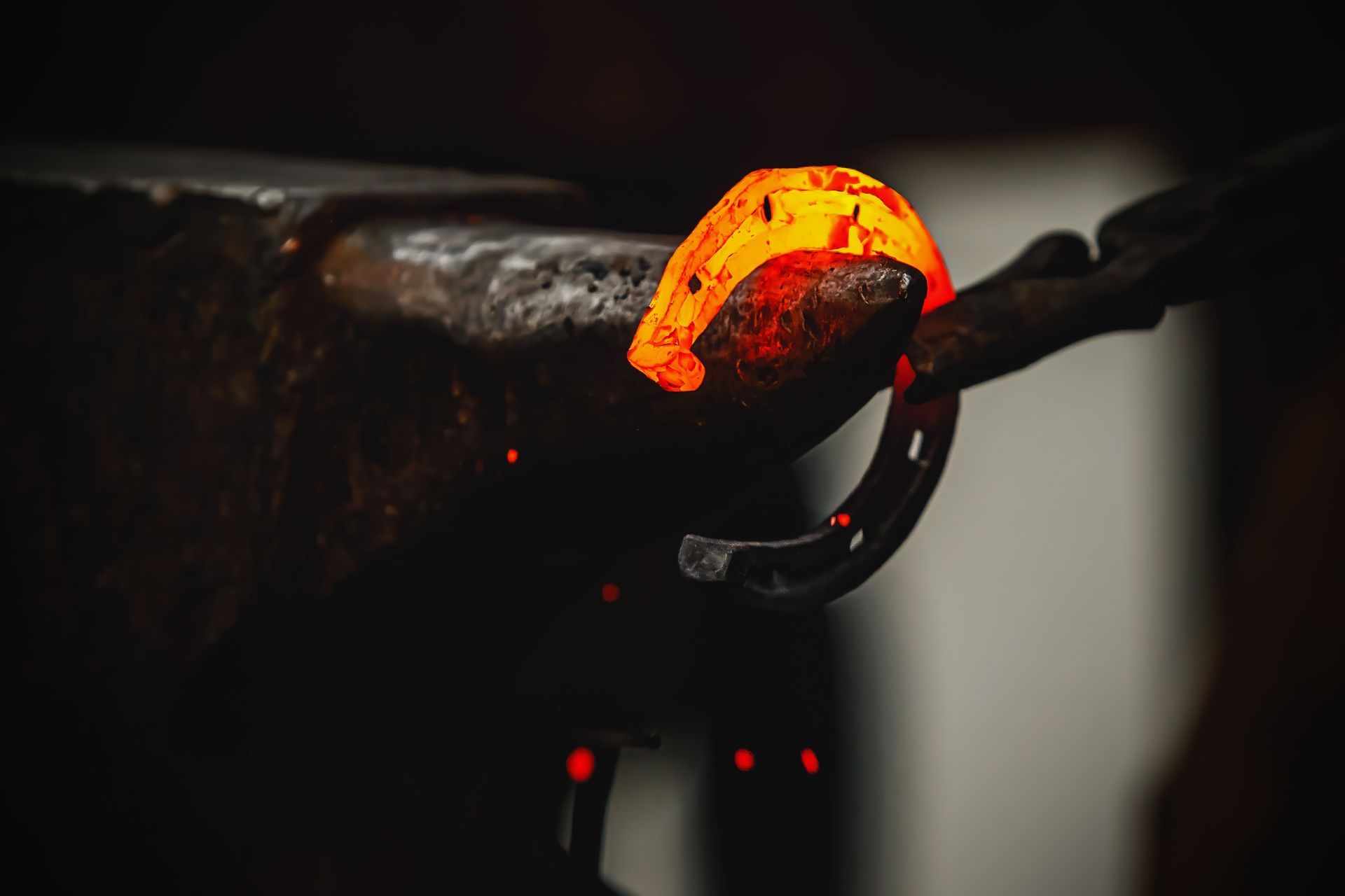 A blacksmith shapes a glowing horseshoe on an anvil in a dimly lit workshop.