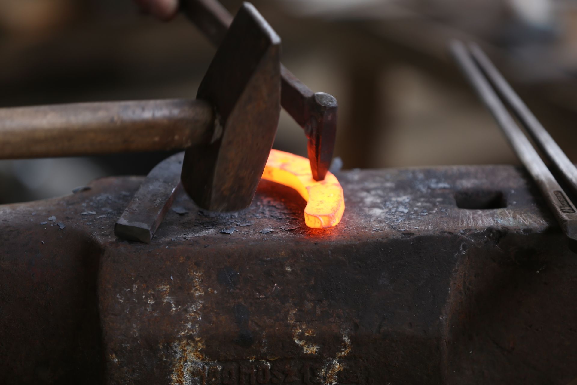 Blacksmith shaping glowing horseshoe with hammer on anvil.