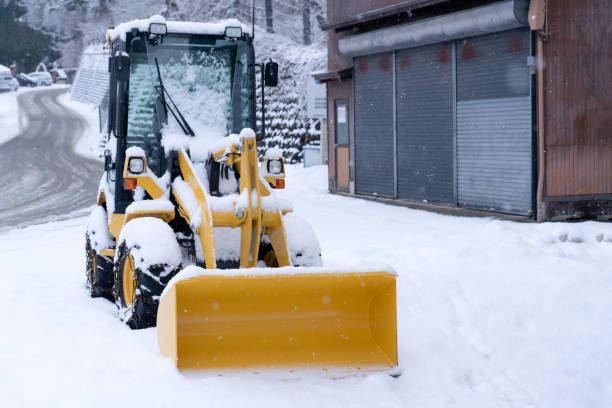 A Yellow Snow Plow Is Sitting in The Snow in Front of A Building.