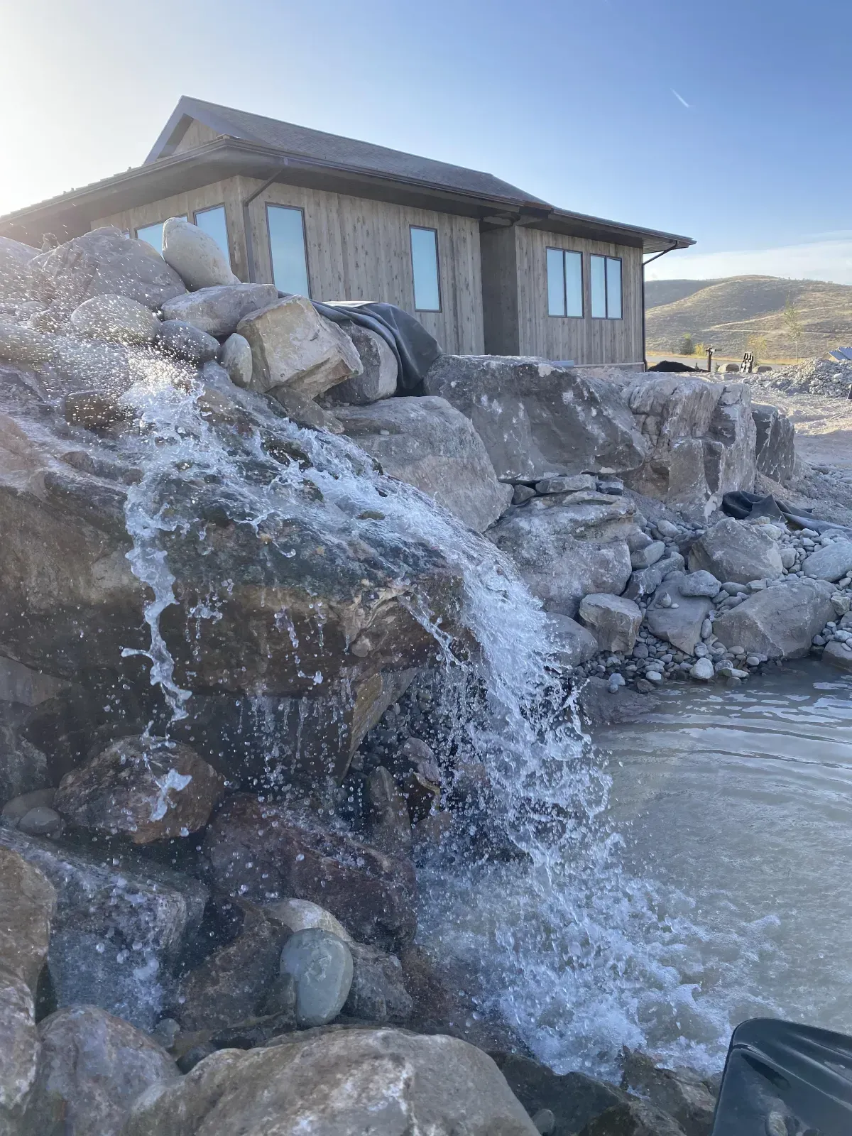 A Waterfall Is Surrounded by Rocks in Front of A House.