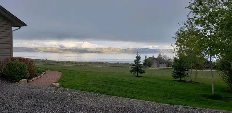 A View of A Lake from A Driveway with A House in The Background.