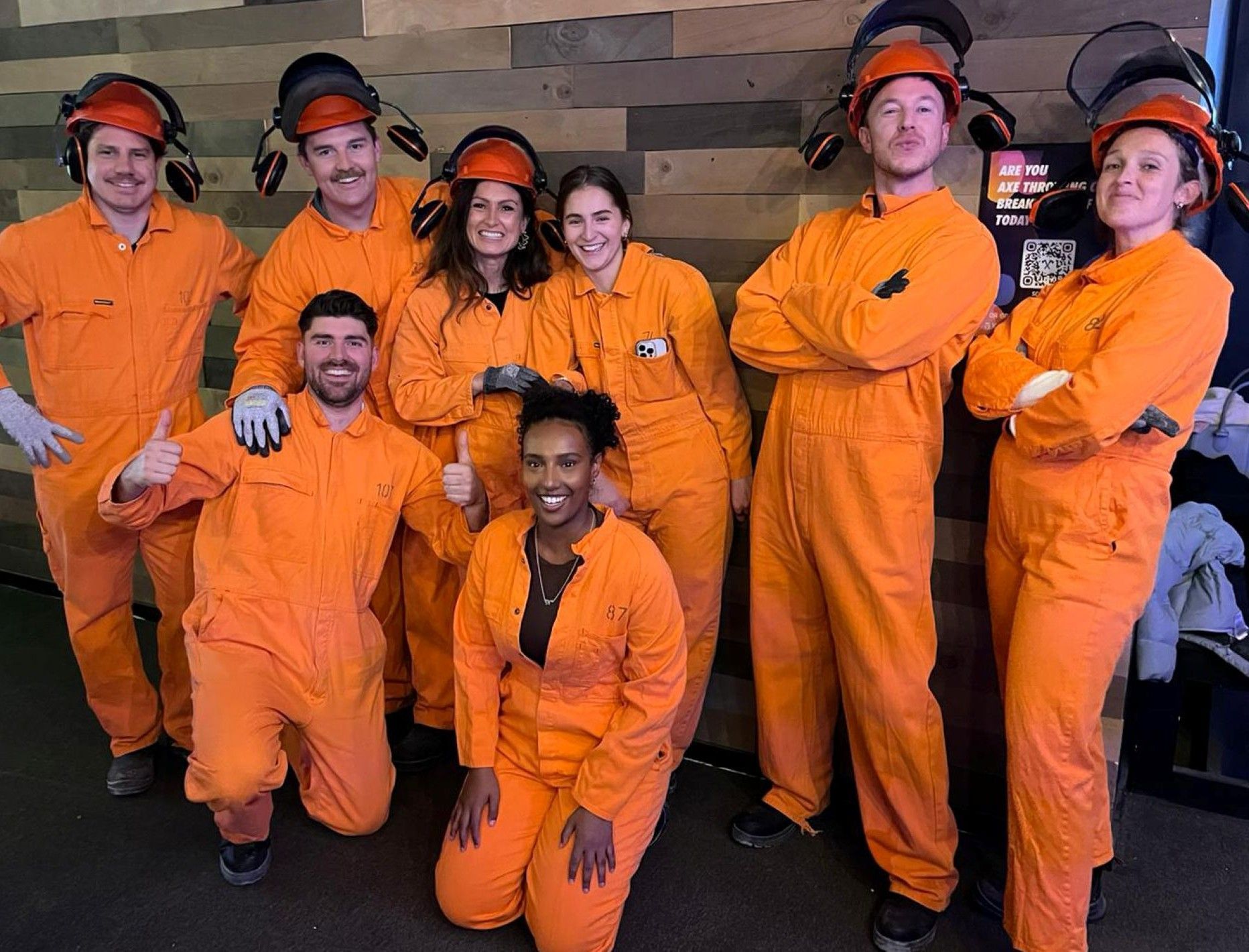 A group of people wearing orange jumpsuits and welding helmets are posing for a picture.