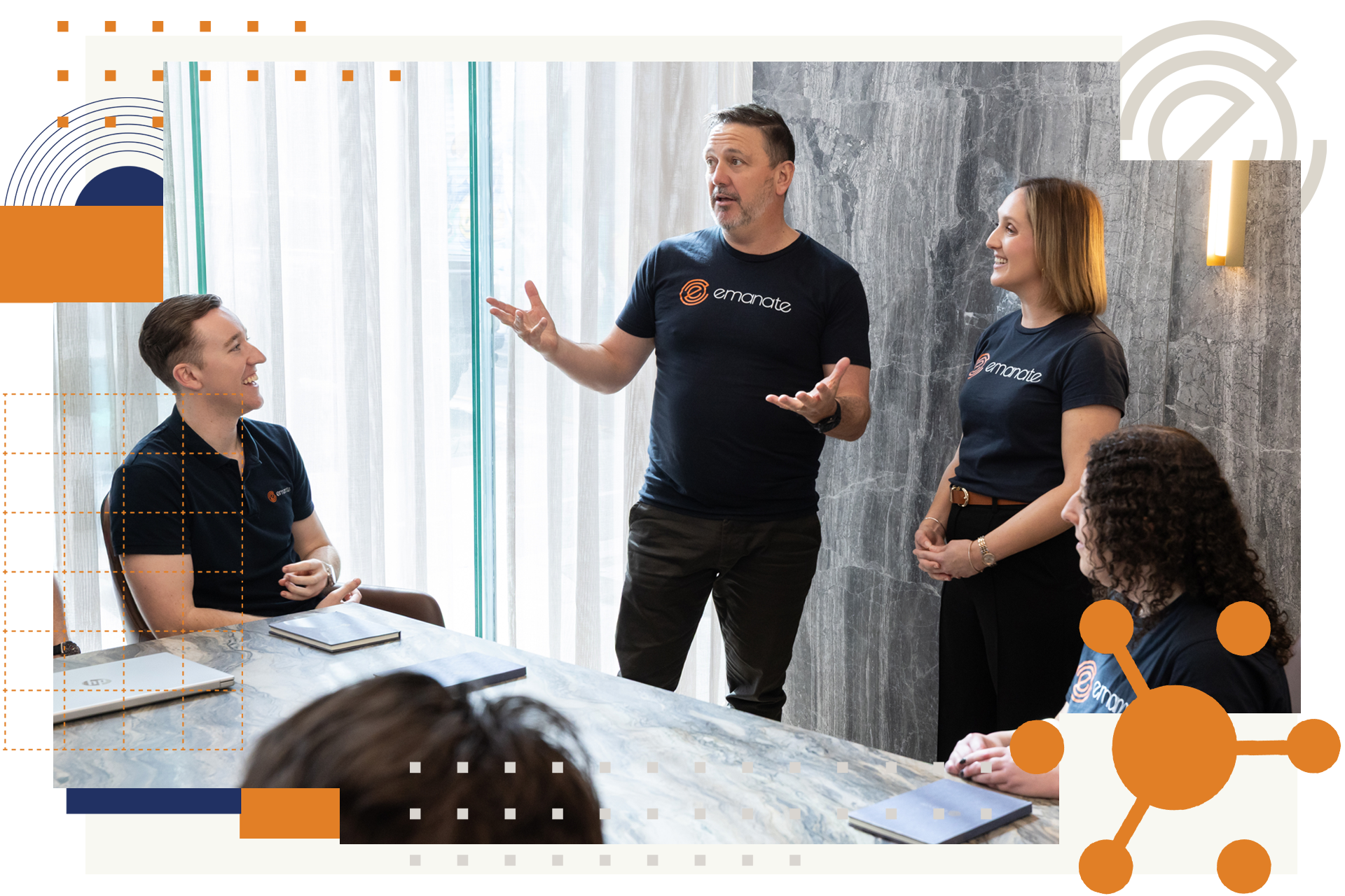 Four people in a meeting, one speaking with hands raised.  Modern office, light and dark tones, laptops on the table.