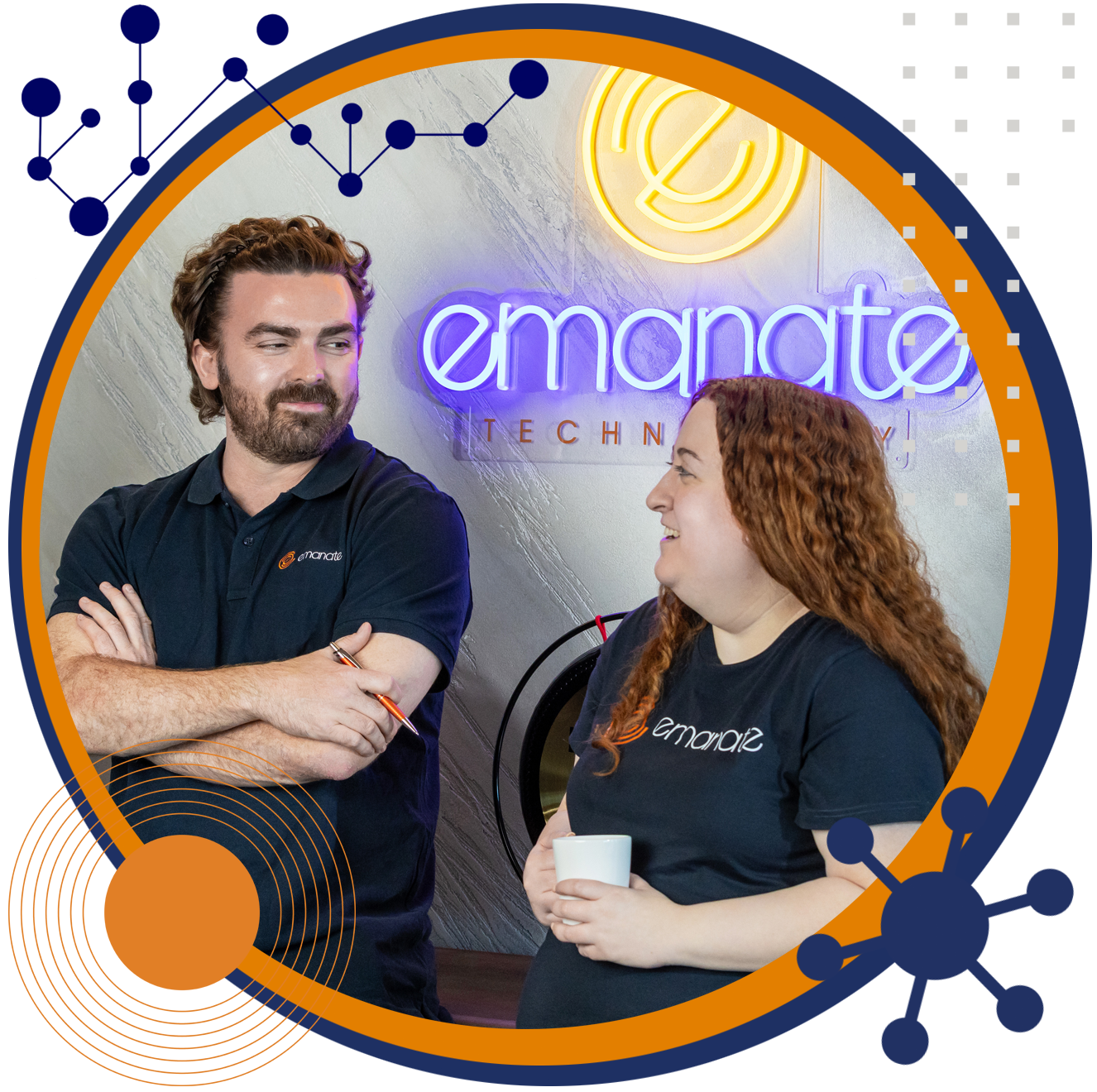 Two people, one with arms crossed, smile and talk in an office with a lit 