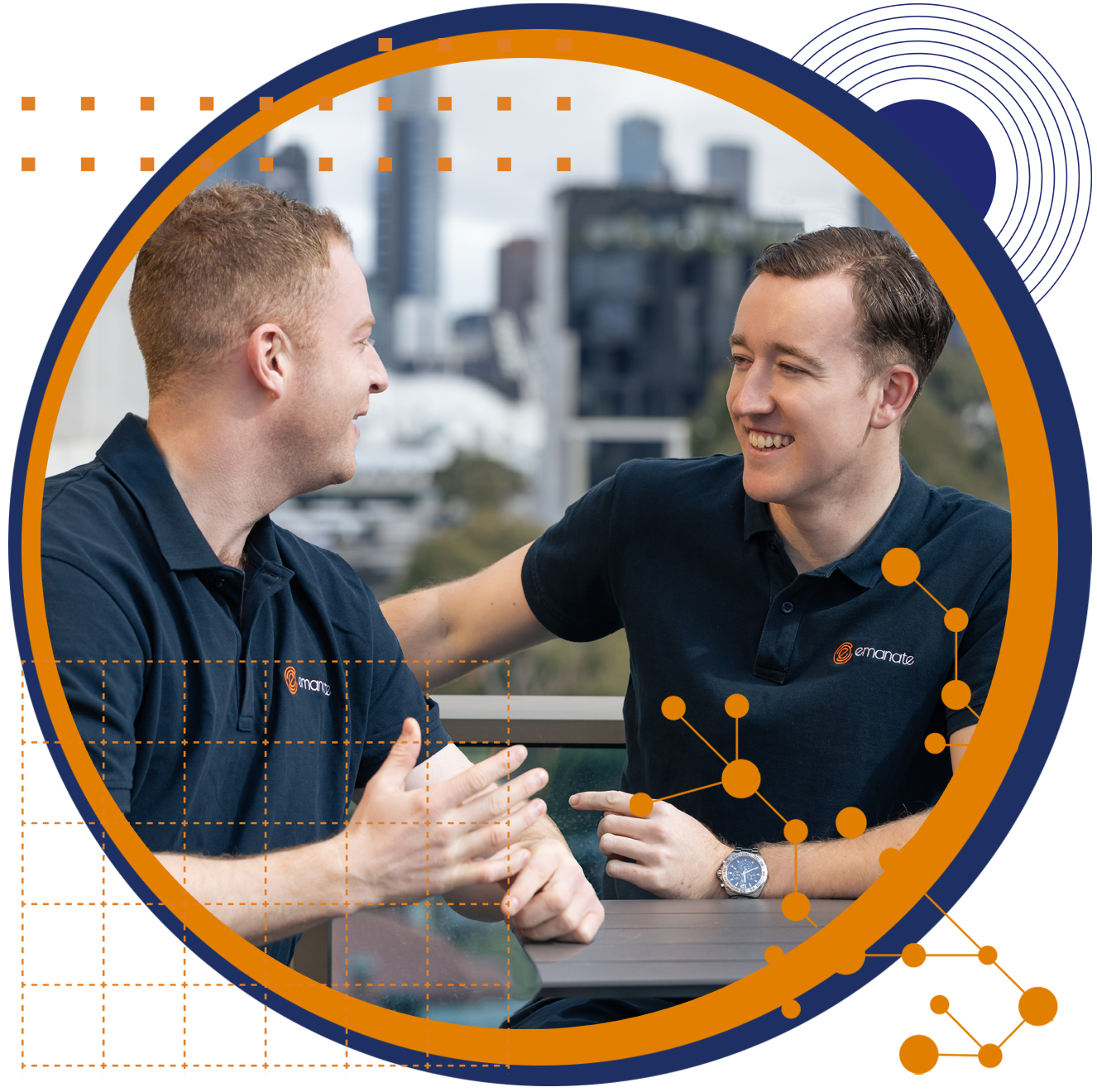 Two men in navy blue shirts laughing outdoors, arm around each other, cityscape in background.