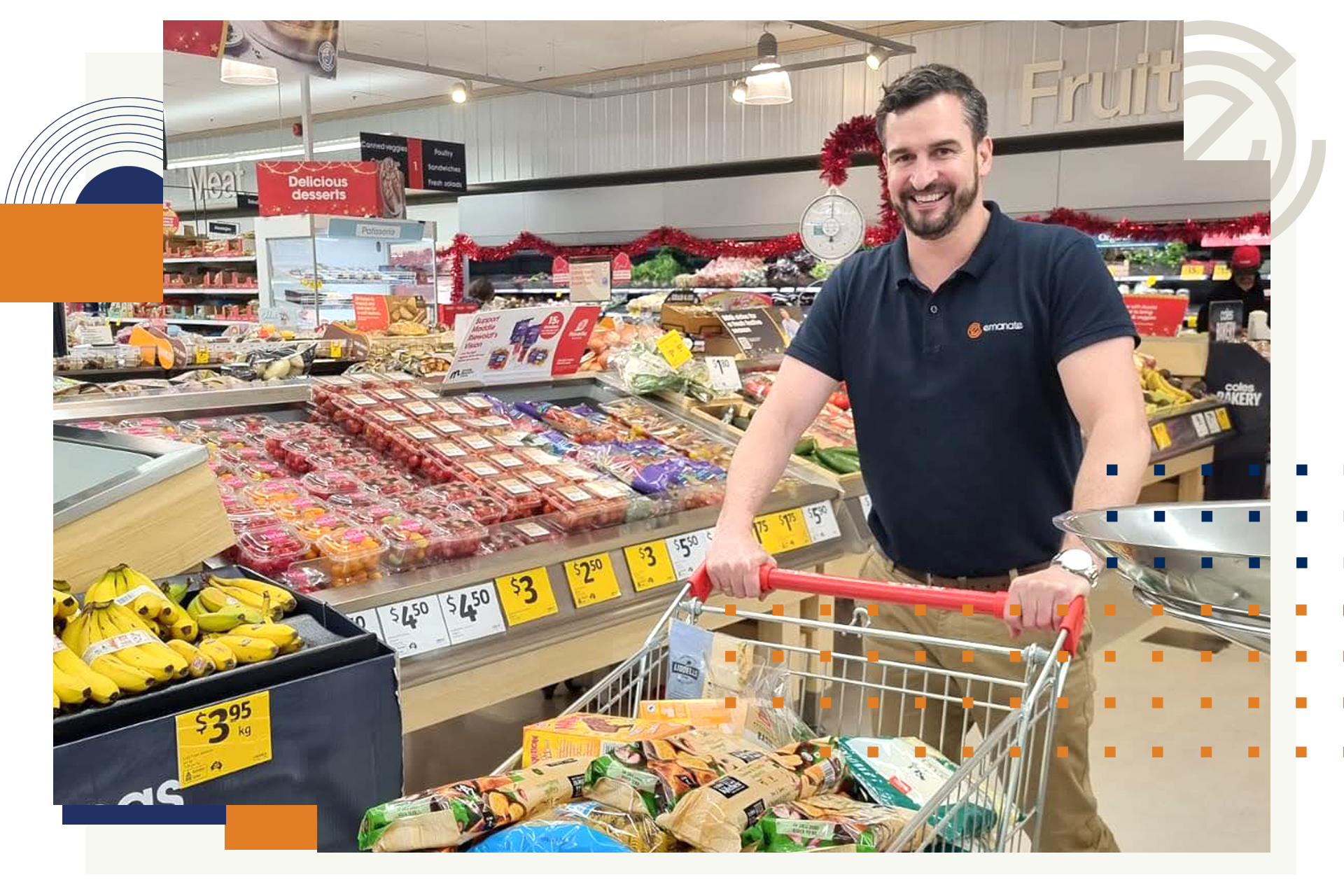 A person with a beard smiles while pushing a shopping cart through the produce section of a grocery store.