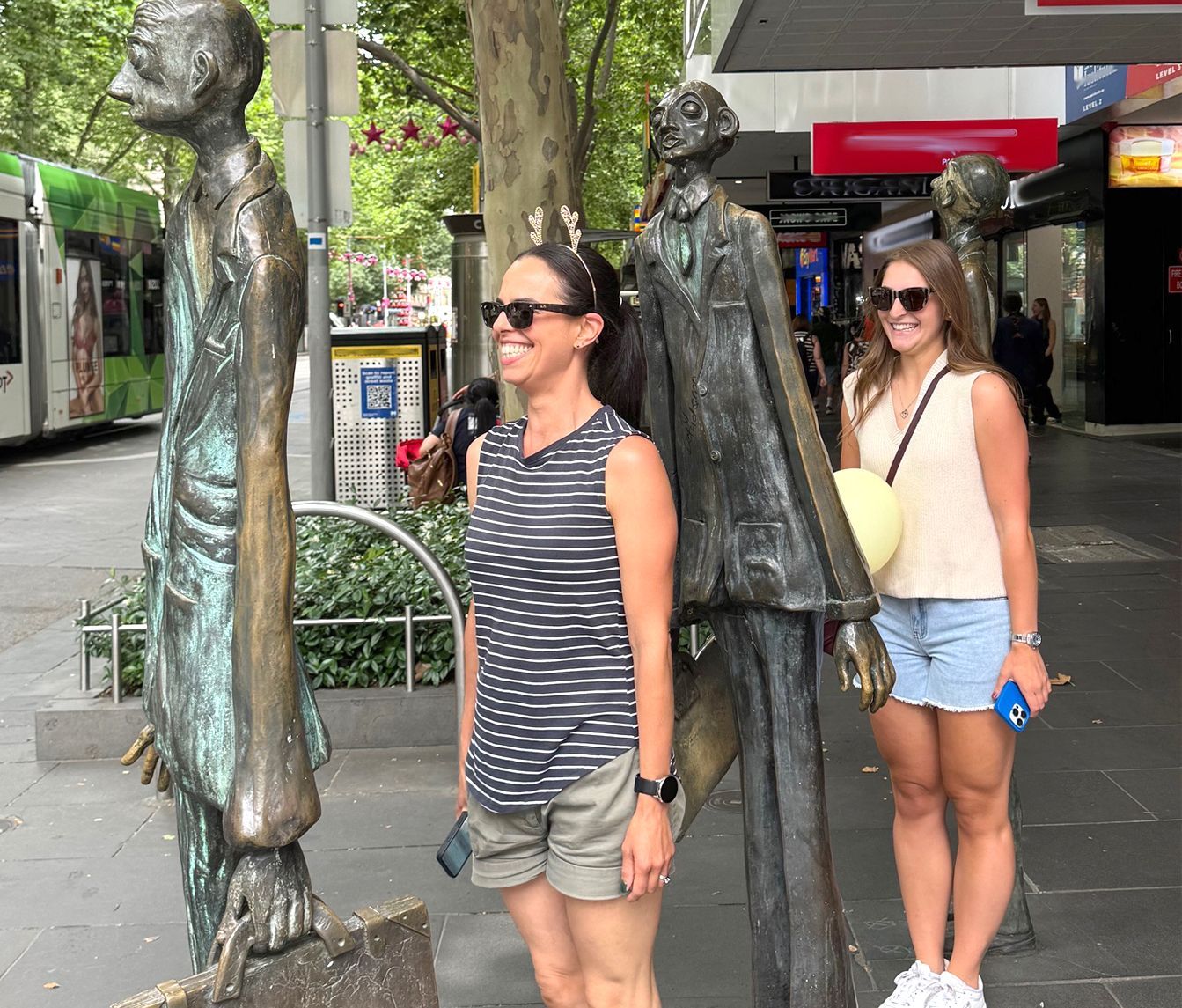 Two women standing next to statues on a sidewalk