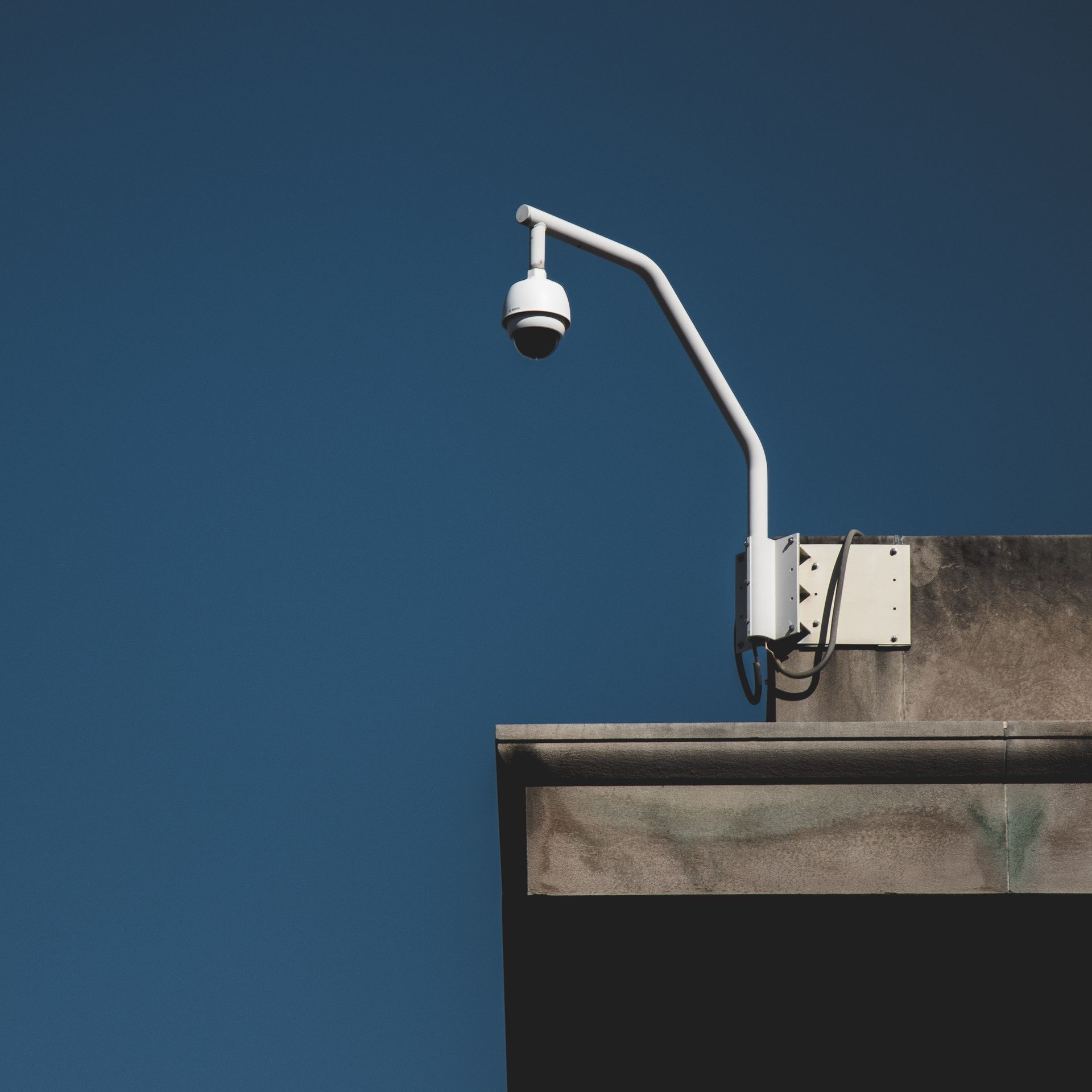 Security camera mounted on a concrete building against a clear blue sky.