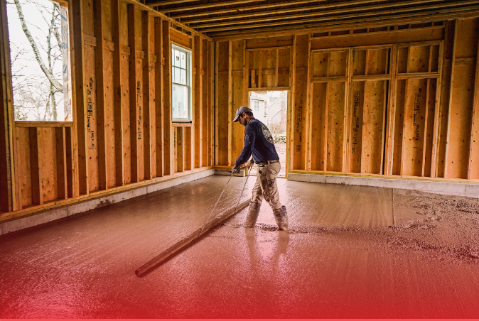 A man is spreading concrete on the floor of a house under construction.
