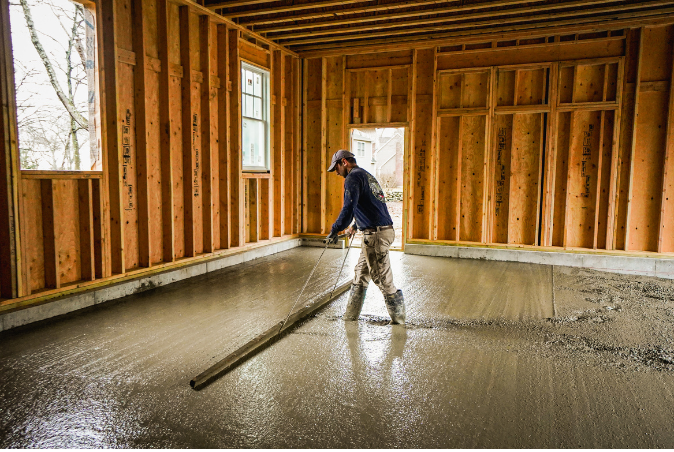 A man is pouring concrete into a room in a house under construction.