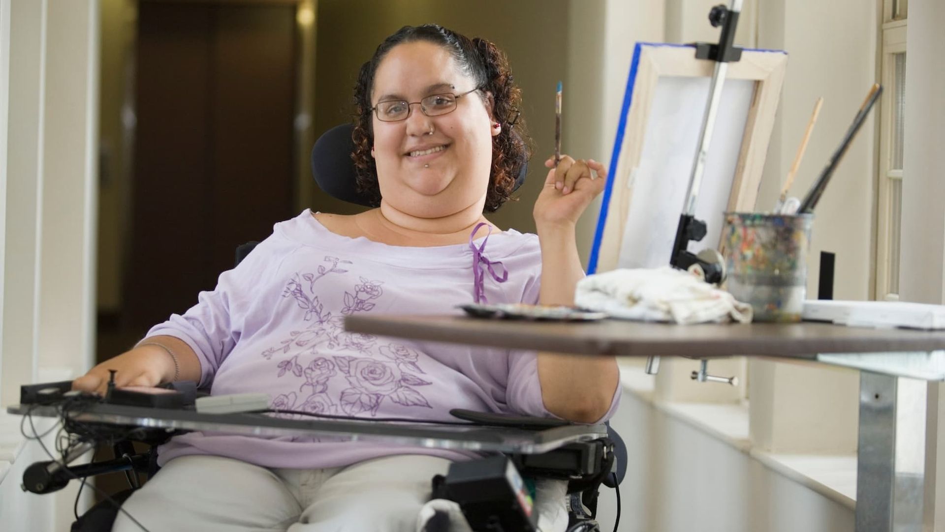 A Woman in A Wheelchair Is Sitting at A Table Holding a Brush — Wonder Care Australia Pty Ltd in Kearneys Spring, QLD