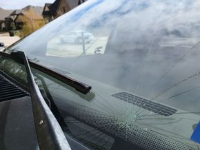 Angled view of the driver side windshield of a blue truck.  There is a large spider web crack that emanates to many cracks outward.