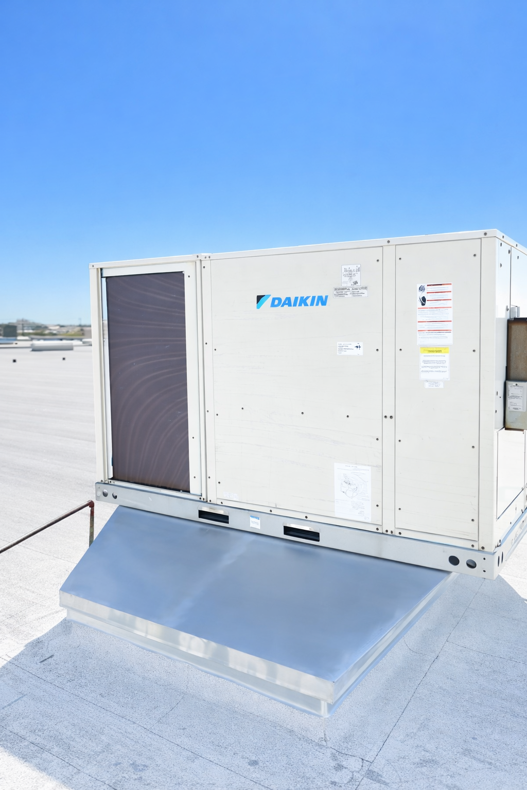 Rooftop HVAC unit on a building, gray metal with black support blocks and piping, set against a blue sky.