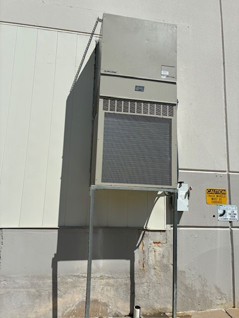 Large wall-mounted industrial HVAC unit on an exterior building wall with visible ducting and conduit.