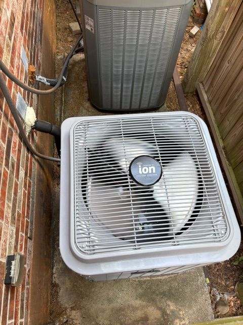 Outdoor air conditioner units beside a brick wall, with a white fan unit in the foreground.