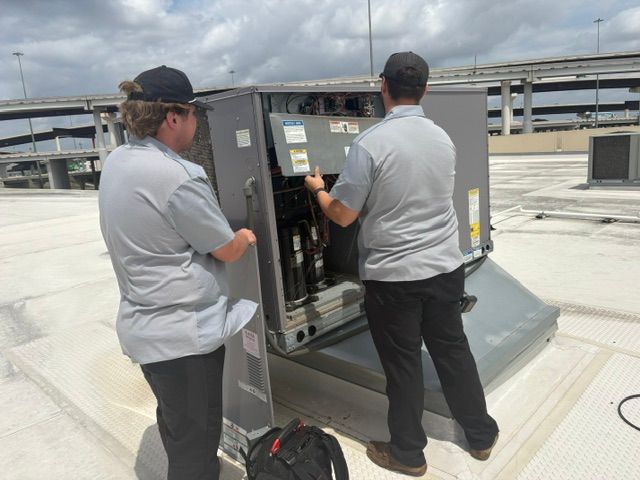 Two workers inspecting an open rooftop HVAC unit on a flat roof