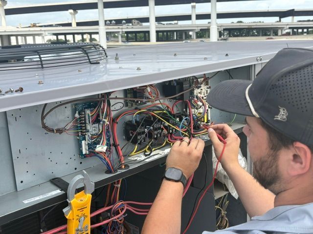Technician working on exposed wiring inside an electrical panel outdoors under a highway overpass