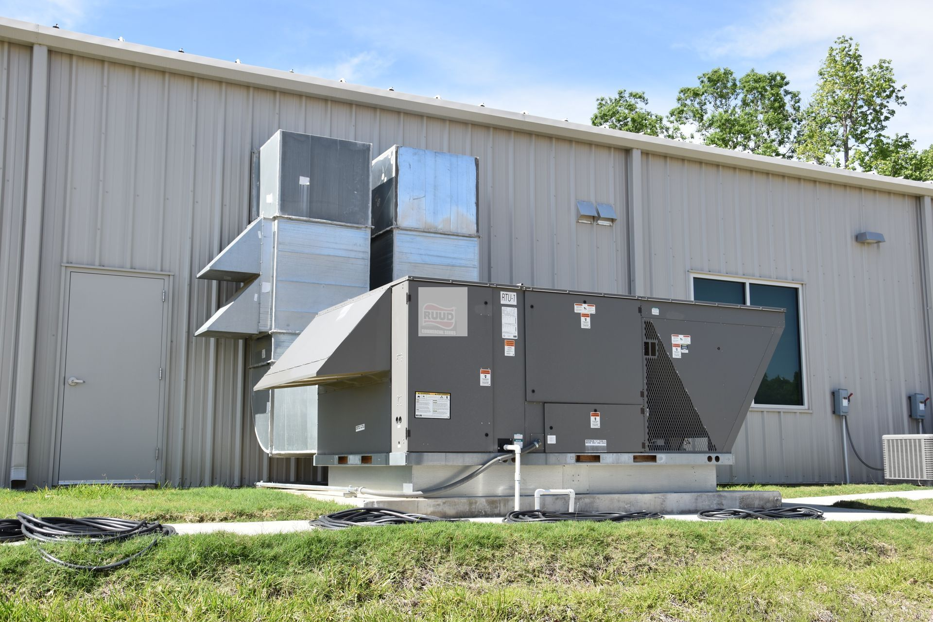 HVAC units on a concrete pad outside a metal building. Air ducts and vents are visible.