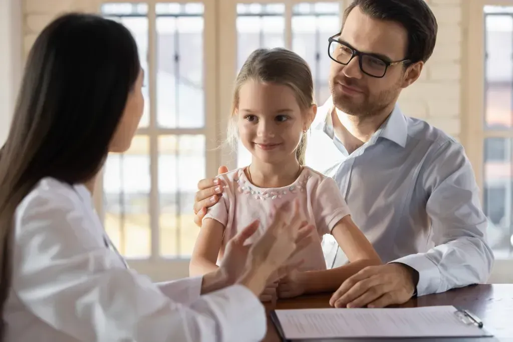 Man and a little girl sitting at a table talking to a doctor.