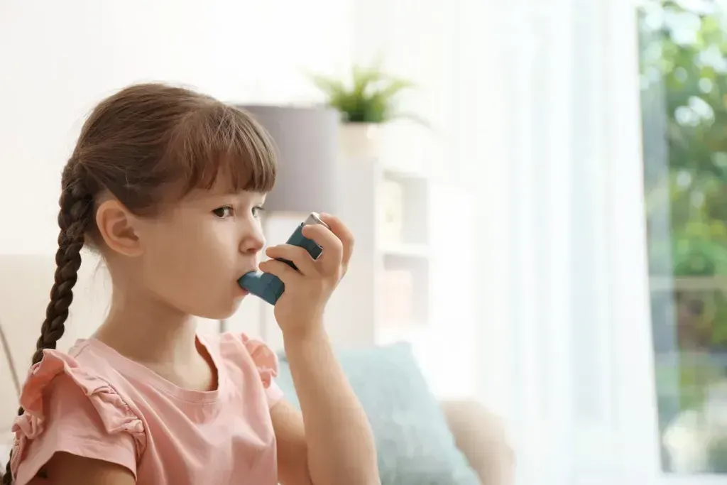 Little girl using an asthma inhaler in a living room.