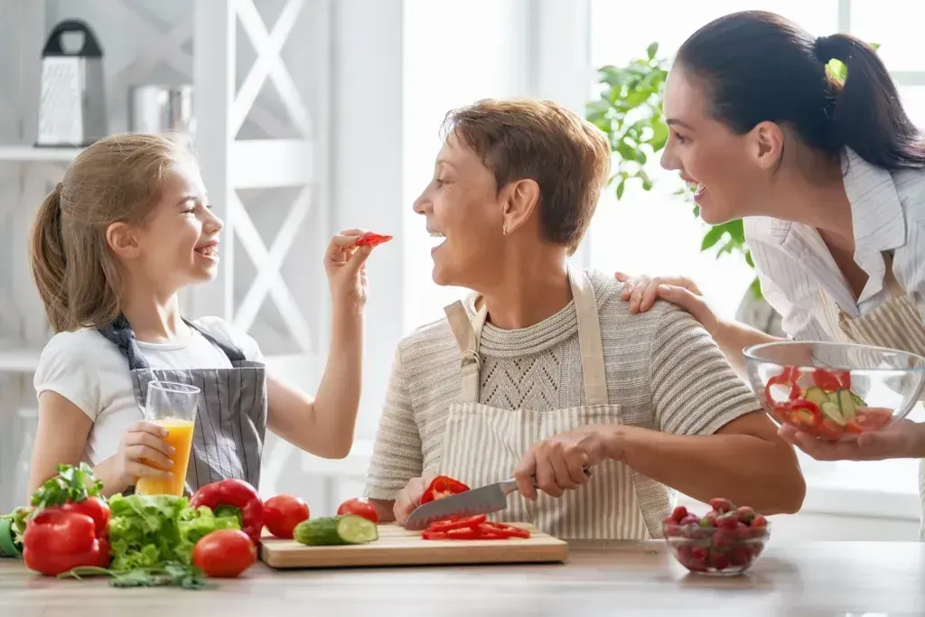 Woman cutting tomatoes on a cutting board while a little girl feeds her.