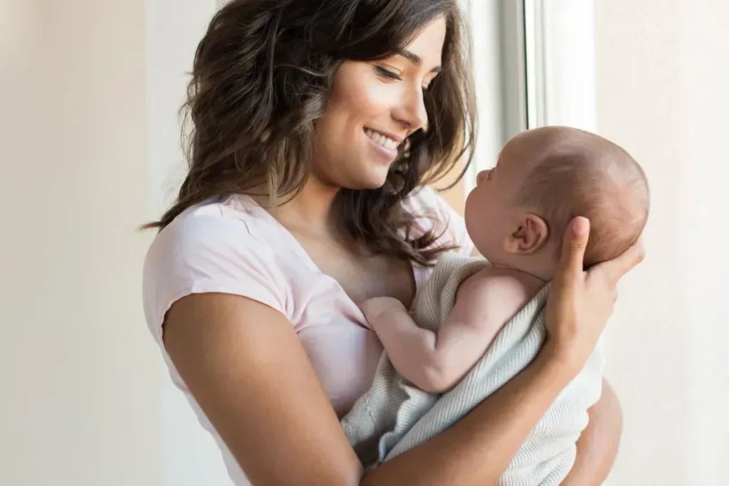 Woman holding a baby in her arms in front of a window.
