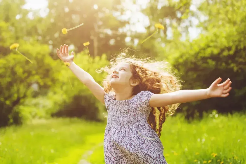Little girl standing in a field with her arms outstretched.