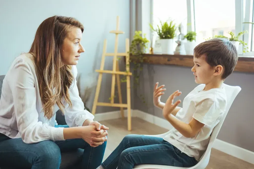 Woman sitting on a couch talking to a young boy who is sitting in a chair.