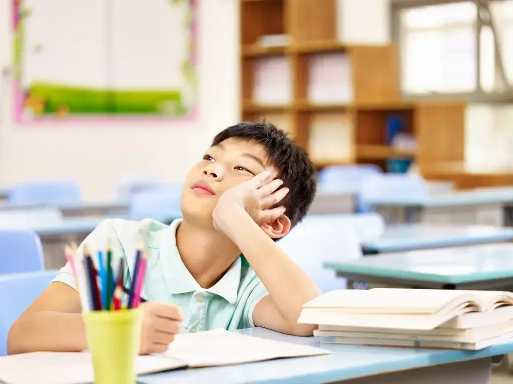 Young boy sitting at a desk in a classroom looking up.