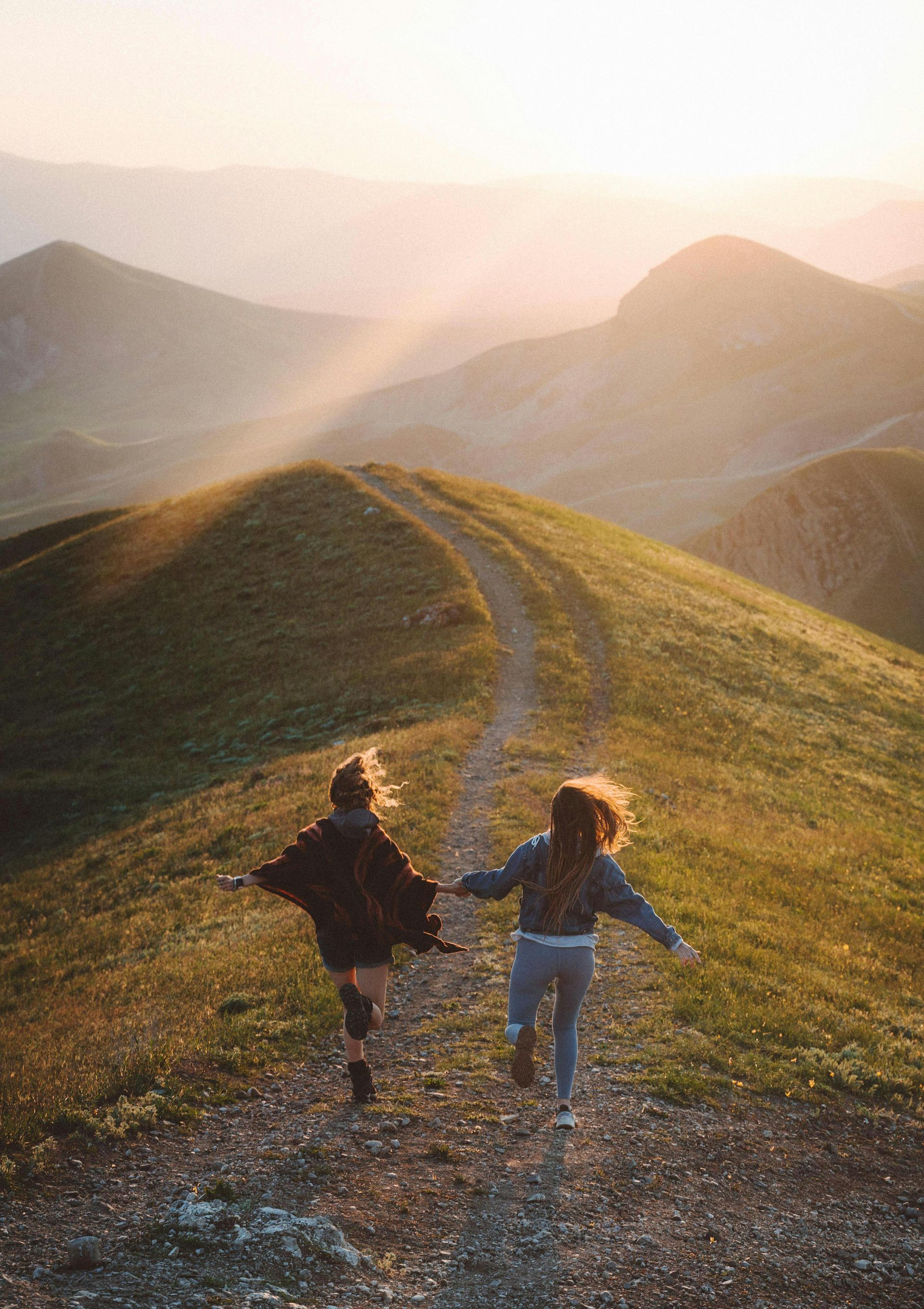 Two people running hand-in-hand along a mountain ridge at sunset.
