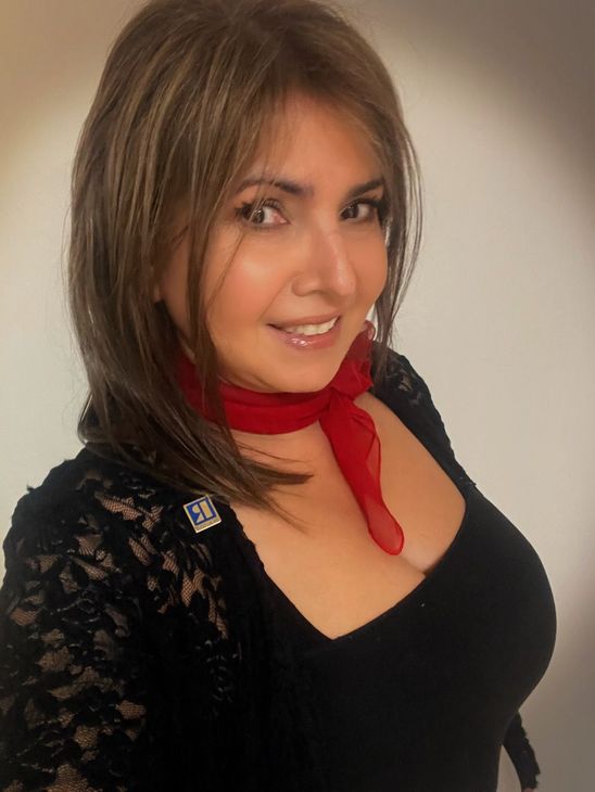 A woman is sitting at a desk with a laptop and a vase of flowers.