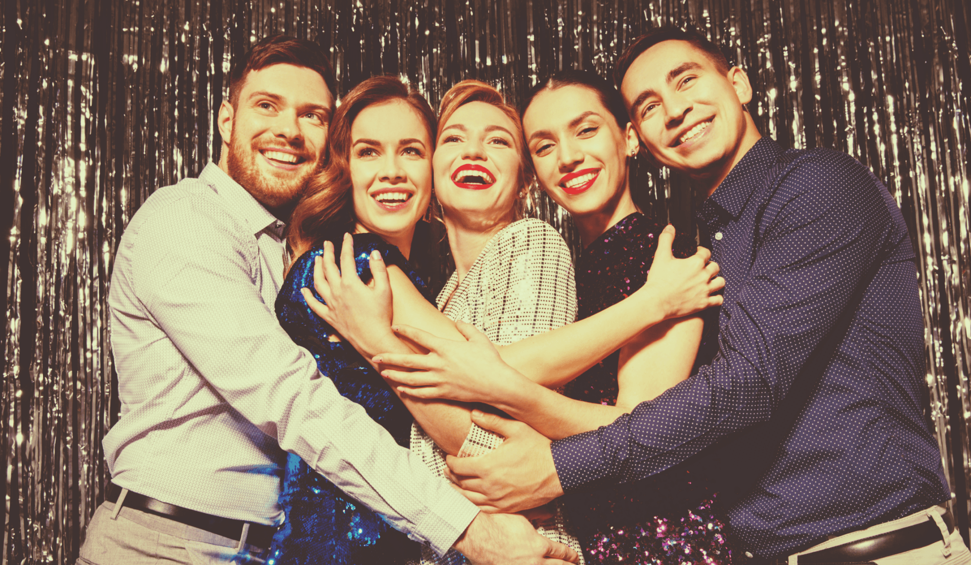 Five people smiling and hugging in front of a shiny, silver backdrop.